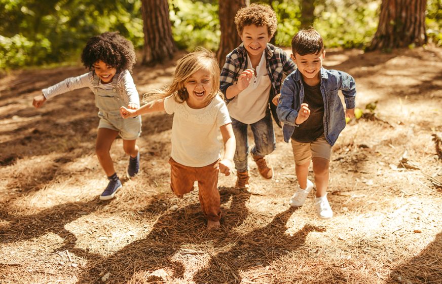 Group of kids running up in the forest. Multi-ethnic children playing together in forest.